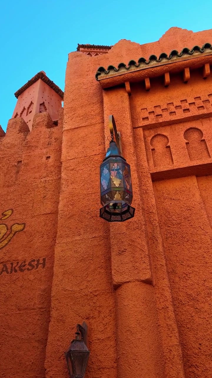 Architettura tradizionale in stile marocchino con lanterne e pareti arancioni texturizzate. Inquadratura dal basso di pareti in stucco arancione con lanterne metalliche ornate e motivi geometrici in un'area a tema