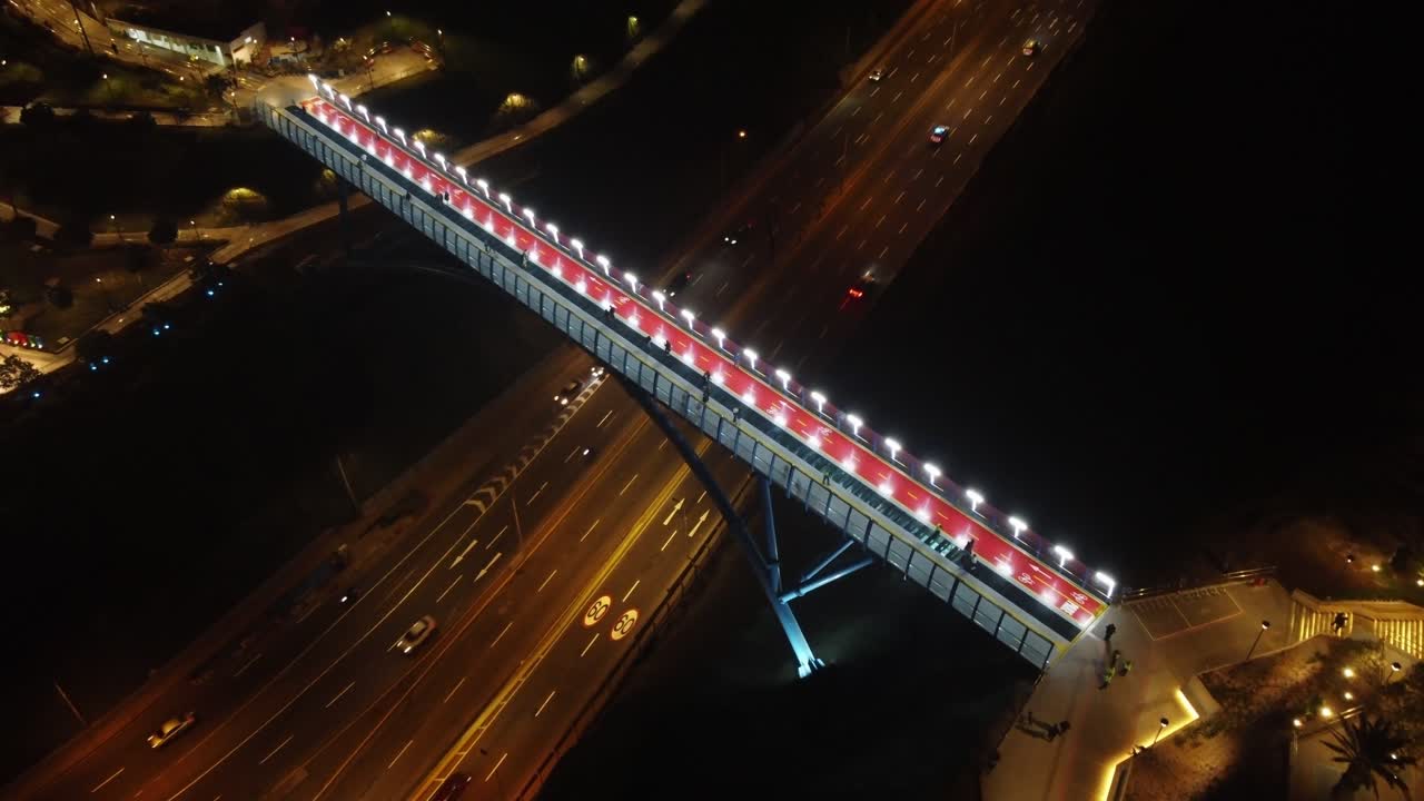 Aerial night time shot of a bridge, above a 4 lane street, connecting two hill top districts of Miraflores and Barranco. Located in Lima, Peru. Drone flies forward and tilts down