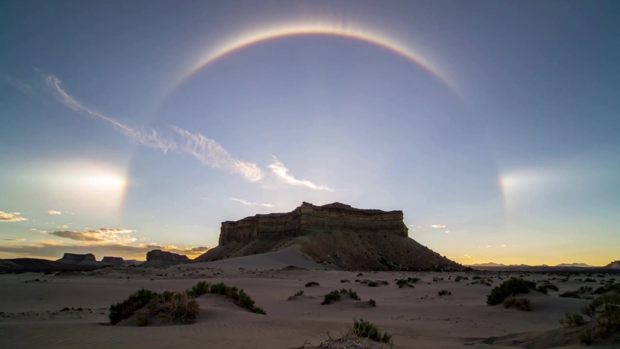 Forming sun dogs and halo above centered flattop mesa over rippled sand dunes, sun low refracting