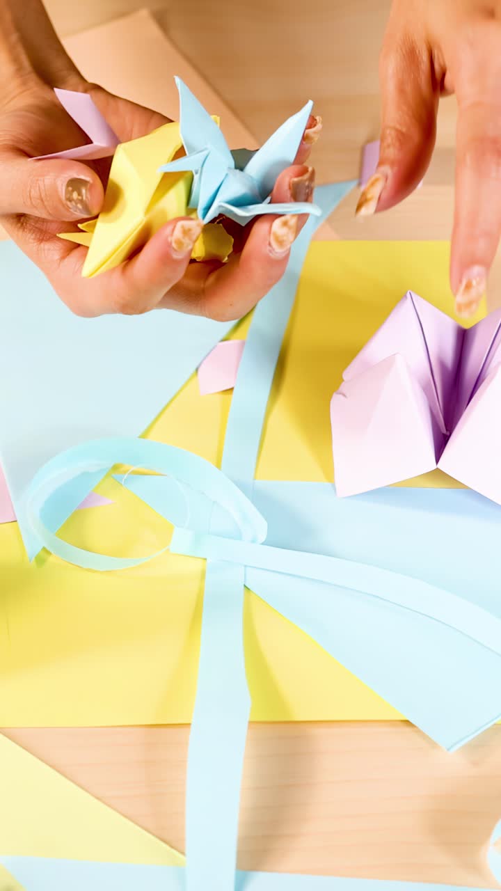 Person arranges colorful origami cranes on pastel-wrapped gift box under bright, even lighting