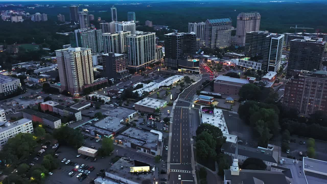 Dusk scene in american town with towers and skyline. Intersection leading into city center. Forest landscape in background. Atlanta, Georgia, USA. Aerial top down flyover.