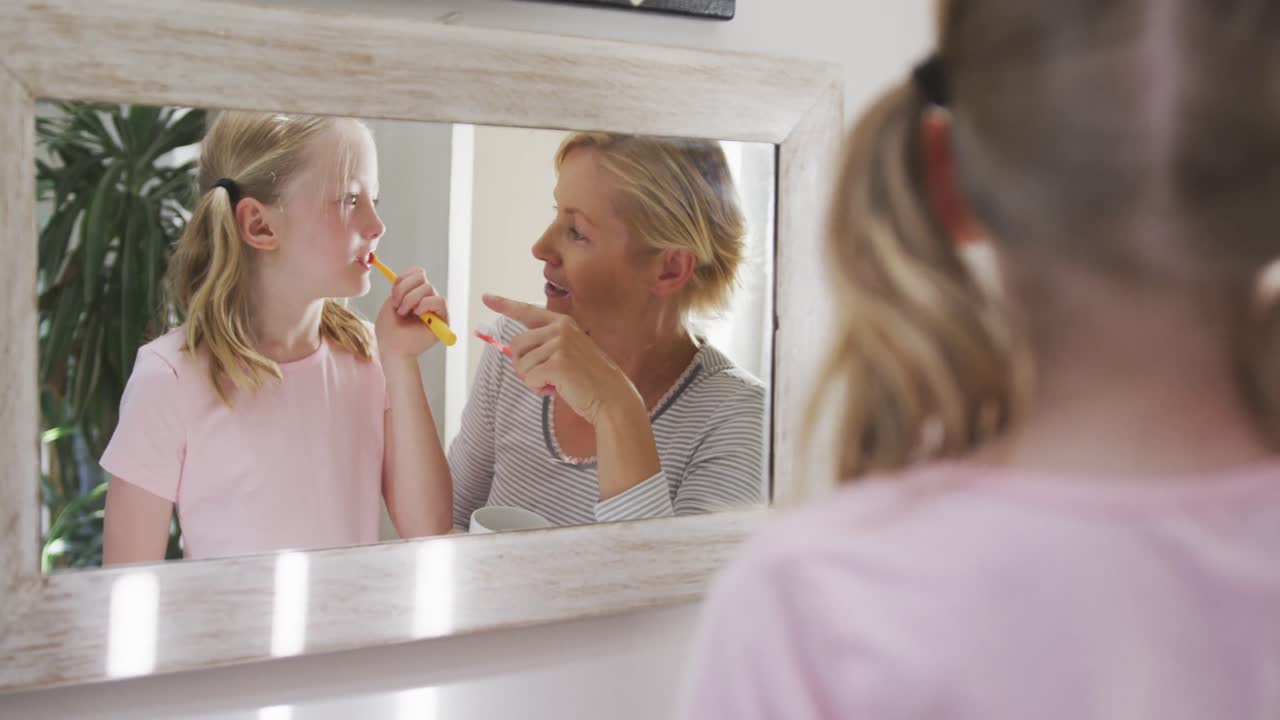 Over the shoulder view of Caucasian woman and her daughter brushing their teeth