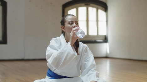 vista frontal de una chica alegre bebiendo agua después del entrenamiento de karate