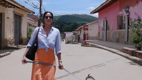 latina in orange dress walks dog on quaint street in samaipata bolivia