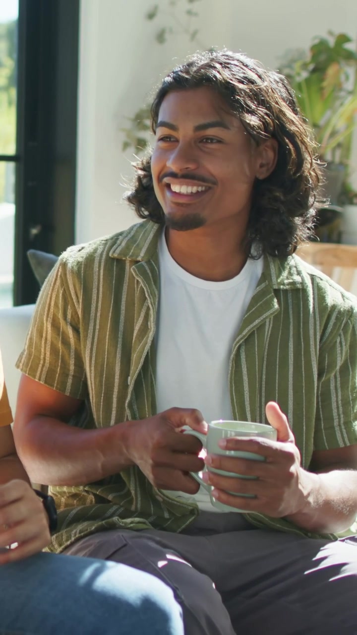 Vertical video: Reacting to off-frame friend, man in green striped shirt holding green mug on couch