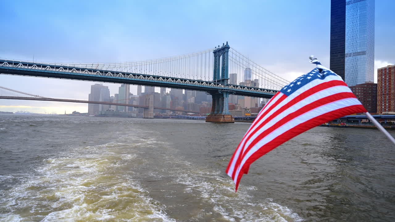 Ponte di Manhattan e skyline di New York visti dal fiume. Vista del Ponte di Manhattan sull'East River con la bandiera degli Stati Uniti che sventola in primo piano su una barca.