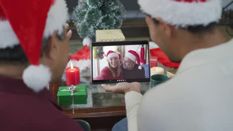 Padre-E-Hijo-Birraciales-Saludando-Y-Usando-Una-Tableta-Para-Una-Videollamada-Navideña-Con-Una-Pareja-En-La-Pantalla