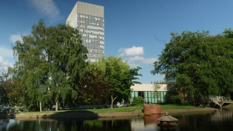 Lapso-De-Tiempo-De-La-Torre-De-Las-Artes-De-La-Universidad-De-Sheffield-Edificio-Alto-Día-Soleado-De-Verano-Con-El-Parque-Weston-En-Frente-Nubes-Moviéndose-En-El-Fondo-Con-Estanque-En-Frente-Y-Torre-Enmarcada-A-La-Izquierda-4k-25p