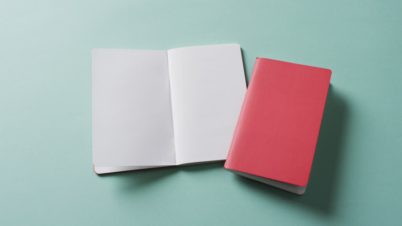 Close up of open blank book and closed red book with copy space on green background in slow motion