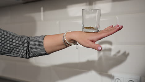 clean glass with beads inside placed on back hand adorned with pearl bracelets, kitchen background with white tiles showcasing delicate hand movement and stylish kitchen deco