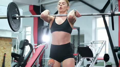 athletic woman performs traction pose, performing exercises with a barbell, lifts a barbell and does strength training in the gym
