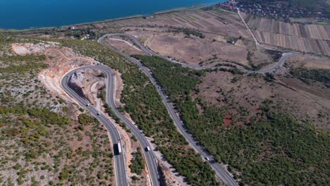 curved road on rocky mountain with cars and bus driving near lake shore in balkans