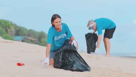 young caucasian man and woman volunteer clean sea beach collect garbage in bags