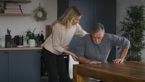 Young-woman-helping-senior-man-stand-up-at-home.