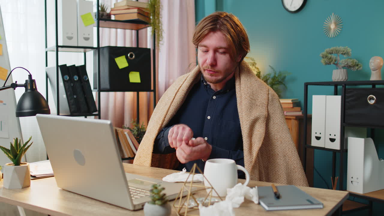 Sick ill young businessman suffering from cold flu or allergy wipes snot working on laptop at office
