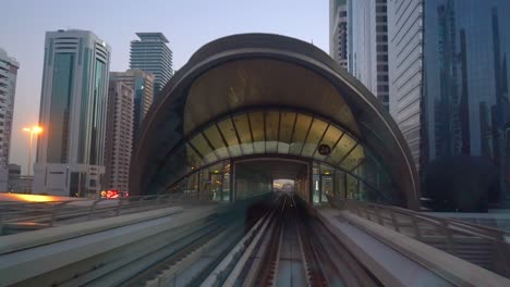 metro de dubai llegando a la estación con una vista del horizonte del centro de la ciudad durante la puesta de sol en dubai, eau