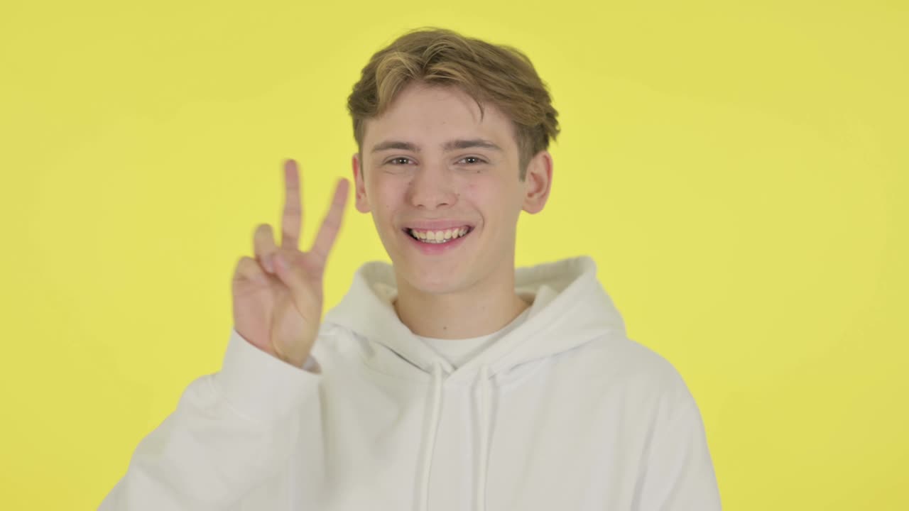 노란색 배경에 승리의 표시를 보여주는 젊은 남자