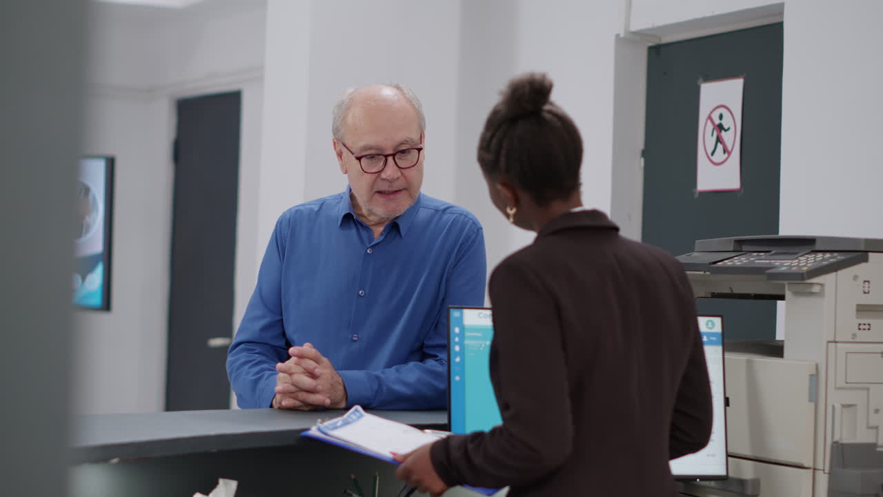 Elderly man talking to African American woman at reception desk
