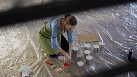 woman in studio workshop open different colors of paint in metal jars on the floor