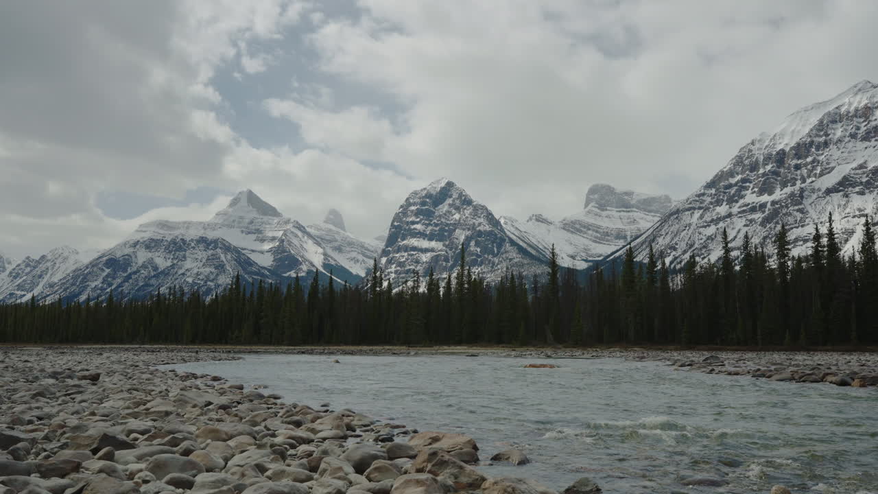 un arroyo y un banco de guijarros, con montañas nevadas a lo lejos, en las montañas rocosas canadienses