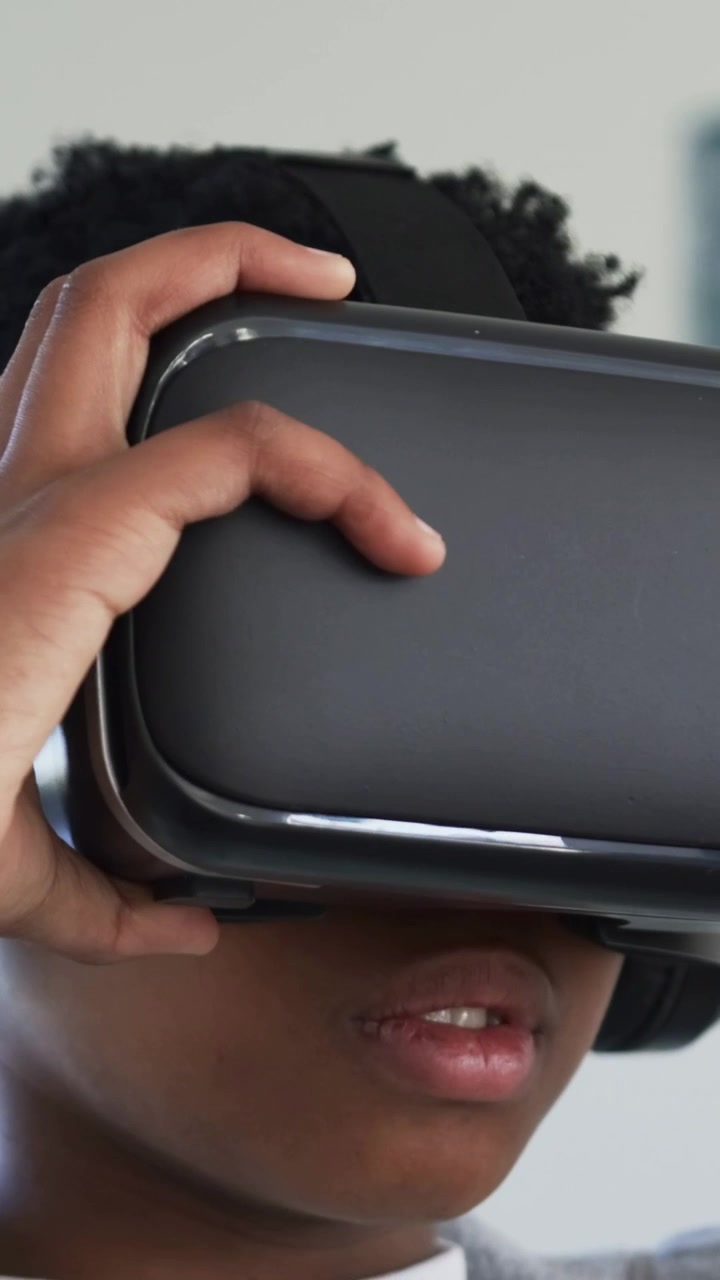 Vertikal video: Teenager i grå sweatshirt placerer VR-headset over øjnene derhjemme for at starte VR