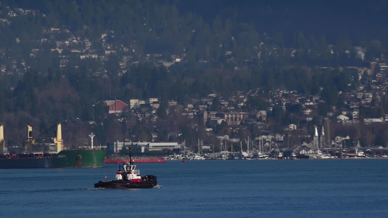 remolcador navegando en el puerto de vancouver para su próximo comando de arrastre con un buque multipropósito verde en el fondo