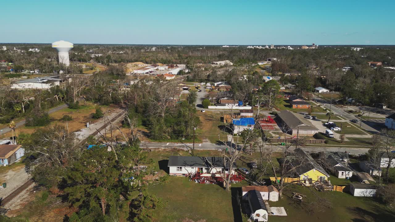 A Small Town With Scattered Houses, Tree-lined Streets, and a Water Tower in the Distance Under a Clear Blue Sky - Aerial Drone Shot