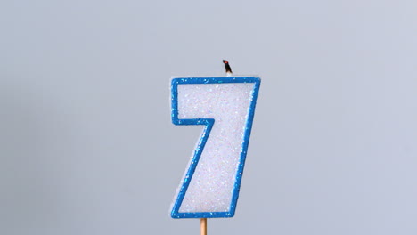 Seven-birthday-candle-flickering-and-extinguishing-on-blue-background