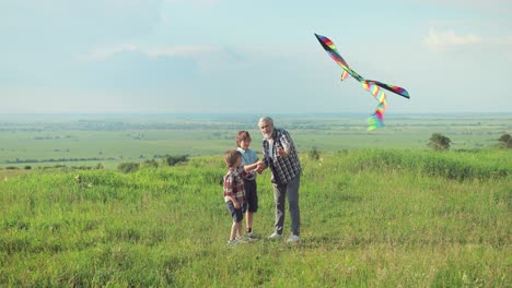 caucasian senior man with his grandchildren in the park while they are flying a kite on a sunny day