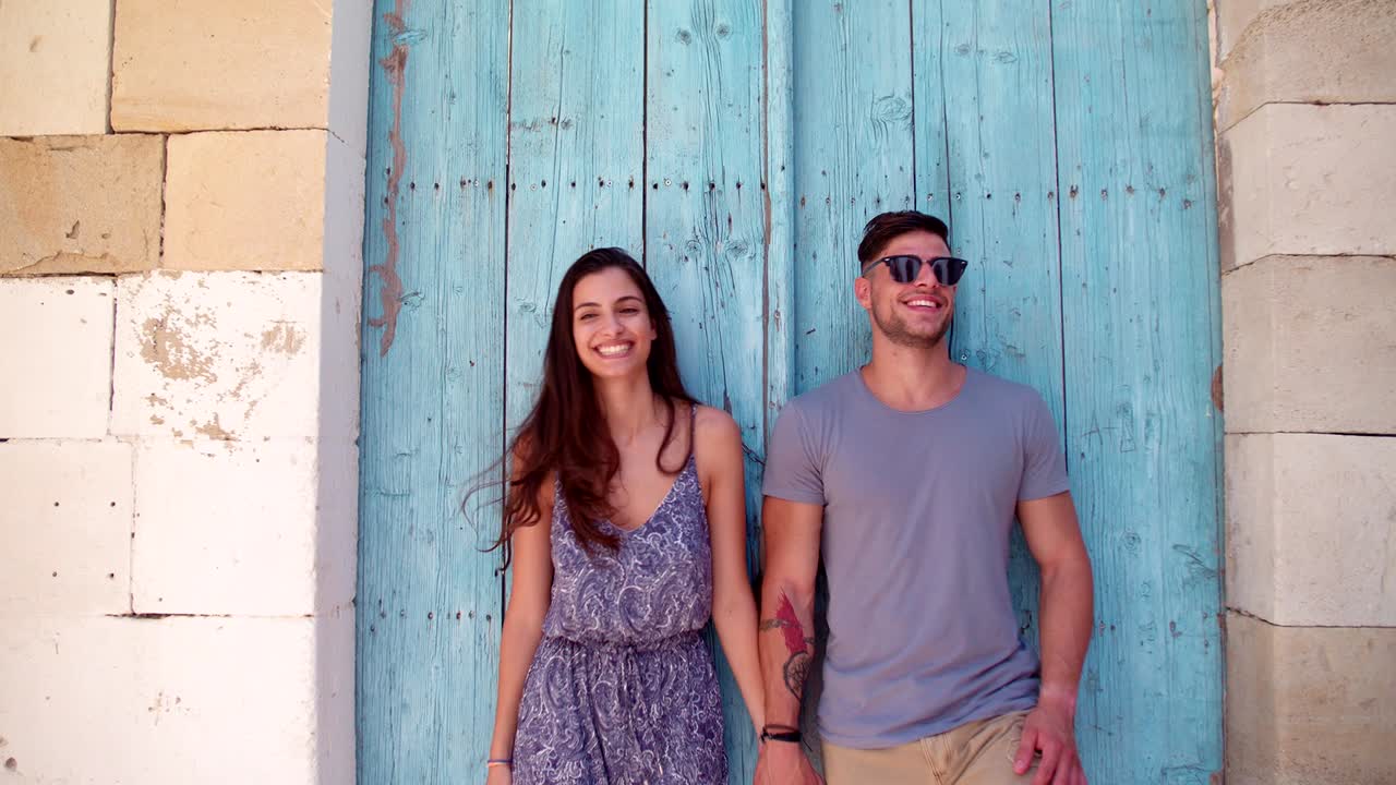 una joven pareja de pie contra una vieja puerta azul en vacaciones en el mediterráneo