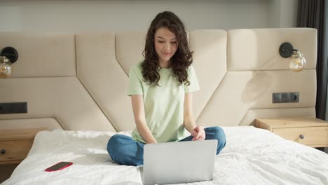 mujer celebrando el éxito en la computadora portátil mientras está sentada en la cama