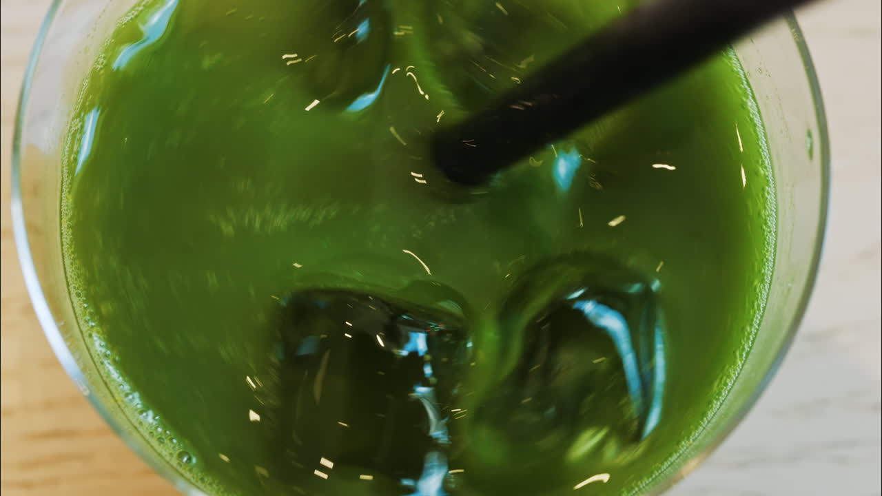 Close up of a hand mixing an iced matcha in a glass with a black straw at a cafe