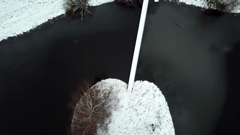 Aerial-top-down-view-on-small-snowy-bridge-from-barren-island-on-a-frozen-lake