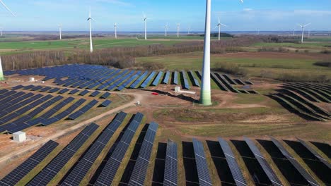 Drone-shot-of-large-power-plant-of-solar-panels-in-Electrum-solar-park-and-wind-turbines-in-a-vast-field-on-a-sunny-day-in-Taurage,-Lithuania