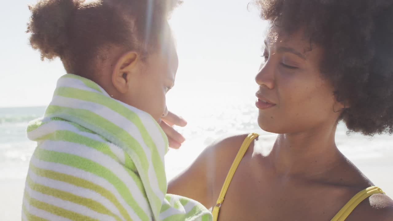 sonriente madre afroamericana toallando a su hija en una playa soleada