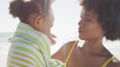 uma mãe afro-americana sorridente a lavar a filha numa praia ensolarada.
