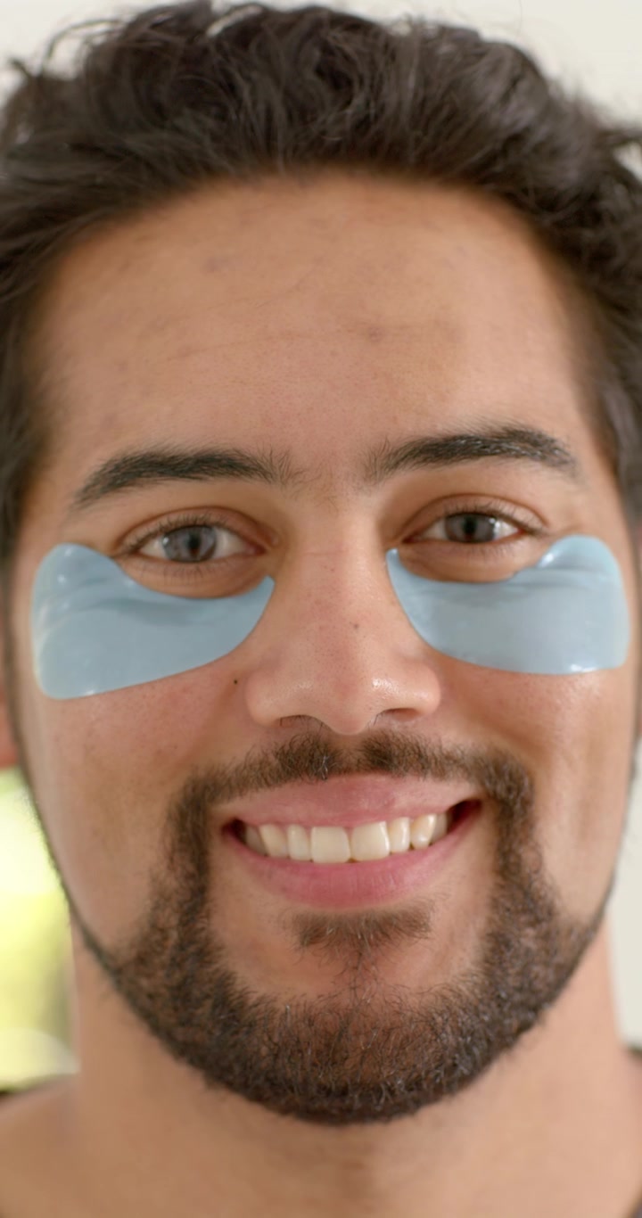 Vertical video: African American man facing camera adjusting undereye patches at sink for eye care