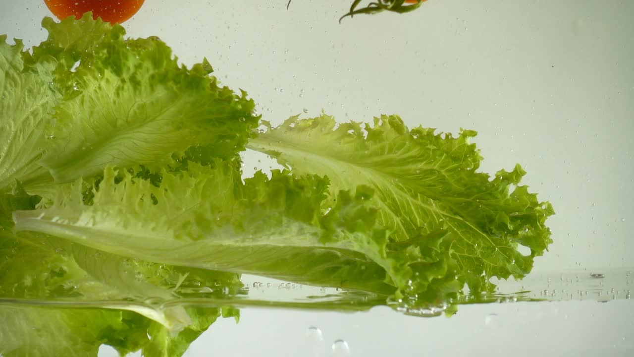Lettuce leaves and cherry tomatoes in water. Slow motion