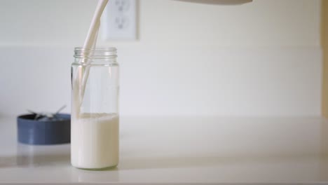 filling a glass jar with homemade, sustainable almond milk