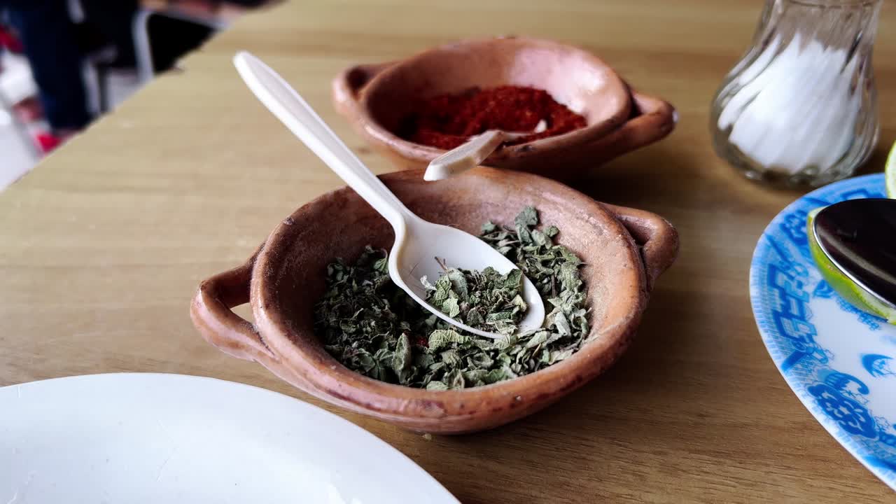 Dried oregano, chili powder, salt and lime on a wooden table, ready to be used in the preparation of a traditional mexican dish, accompanied by a plate with fried tortillas, panning shot
