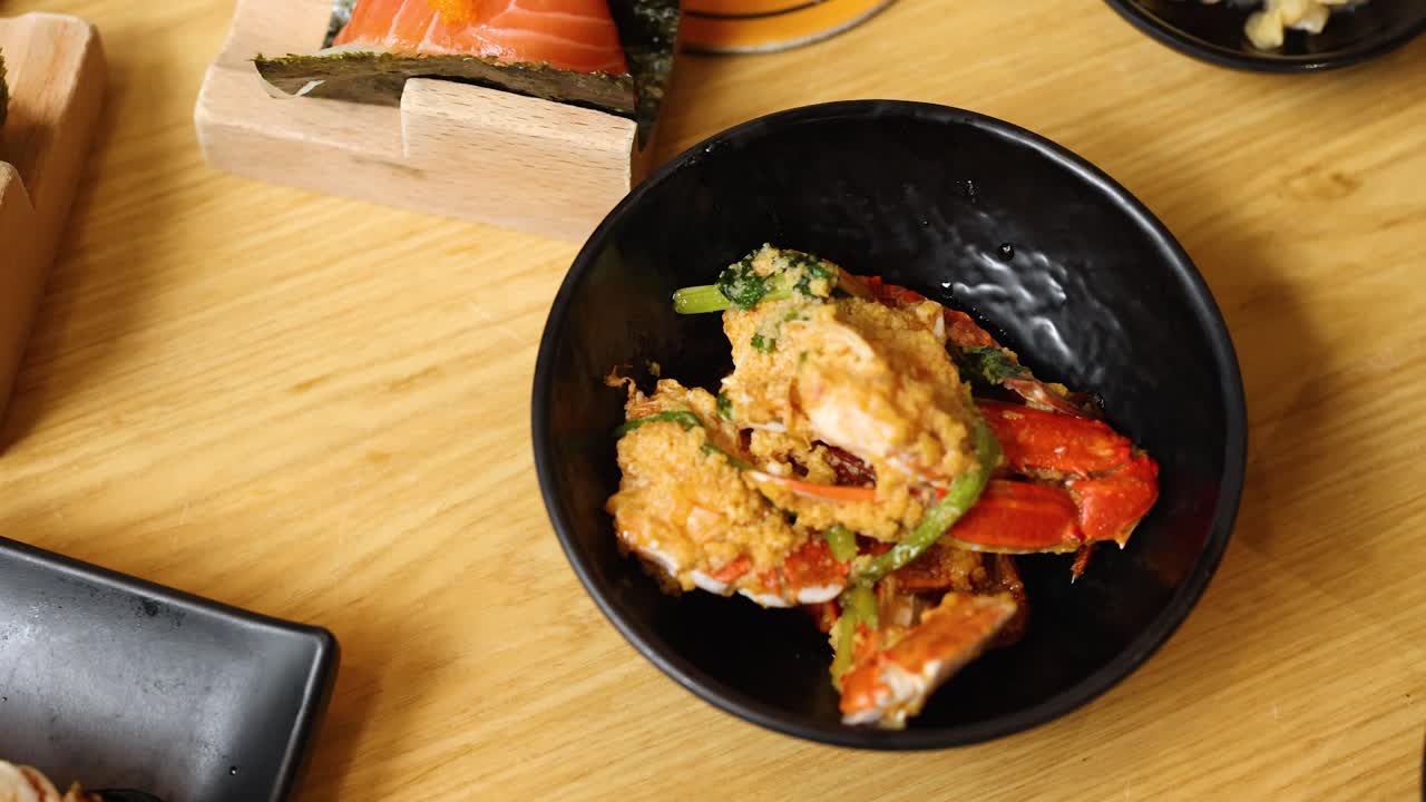 Overhead view of hand reaching for spicy crab dish on wooden table, bright natural lighting