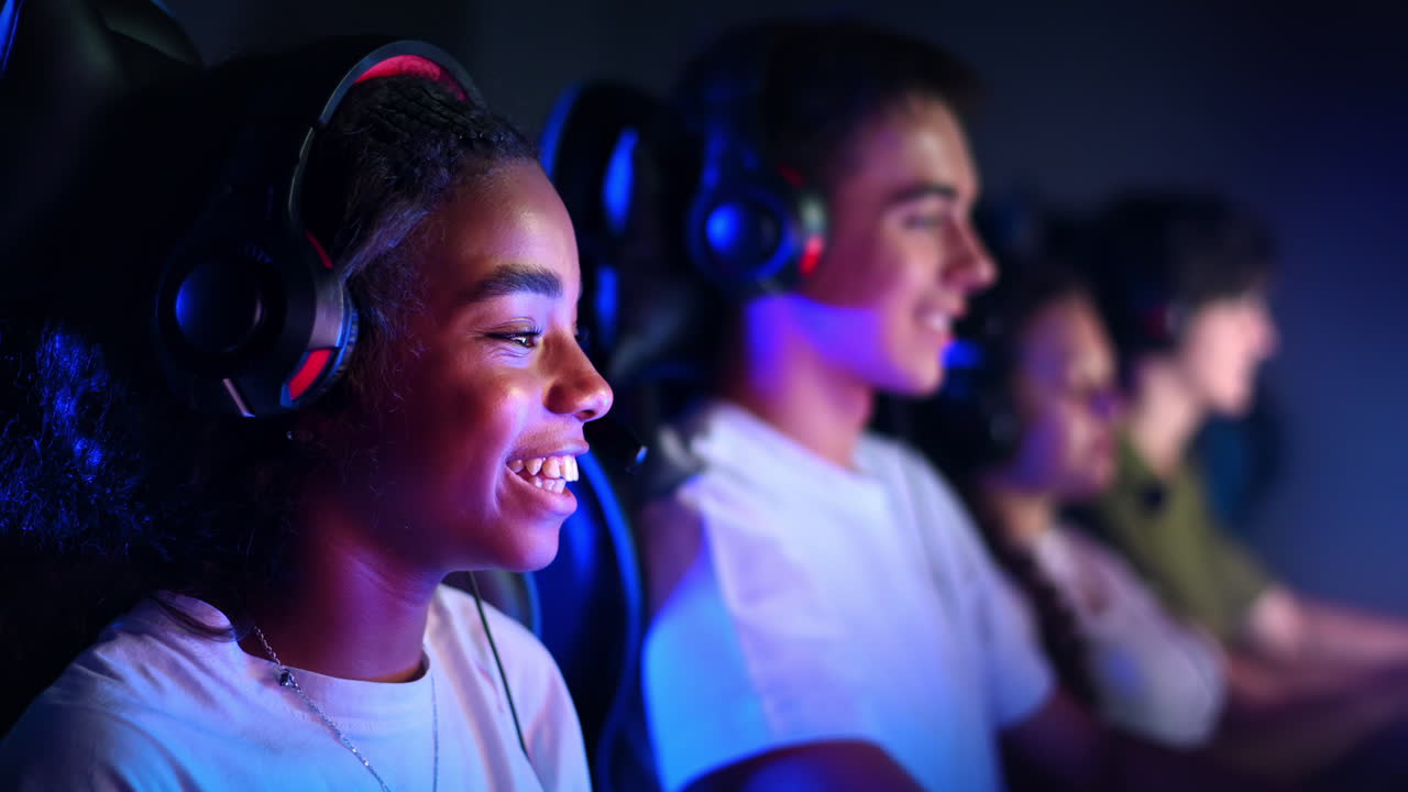White boy and black girl teens in headsets playing video games in video game club with blue and red illumination. Slow motion