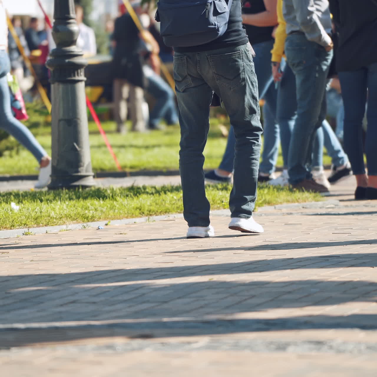 Unrecognizable people walking in the city. Sidewalk and legs of crowds of people moving along slowly in summer. People resting in the city park.