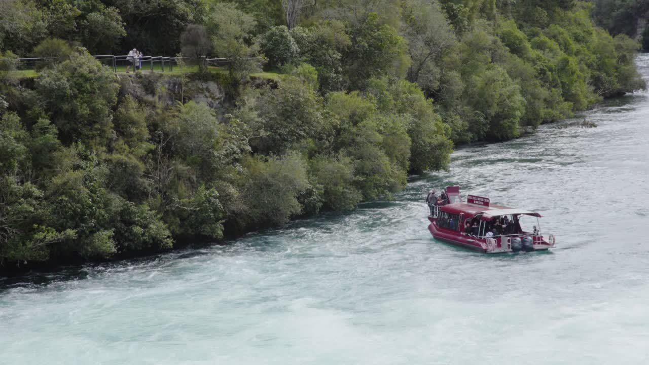 A zoomed in shot of the Huka Falls cruise boat maneuvering in the water with people watching from a lookout