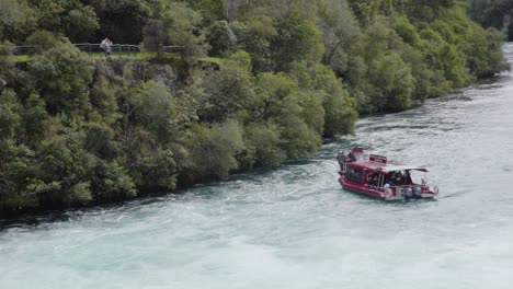 Eine-Herangezoomte-Aufnahme-Des-Kreuzfahrtschiffs-Huka-Falls,-Das-Im-Wasser-Manövriert,-Während-Leute-Von-Einem-Aussichtspunkt-Aus-Zuschauen