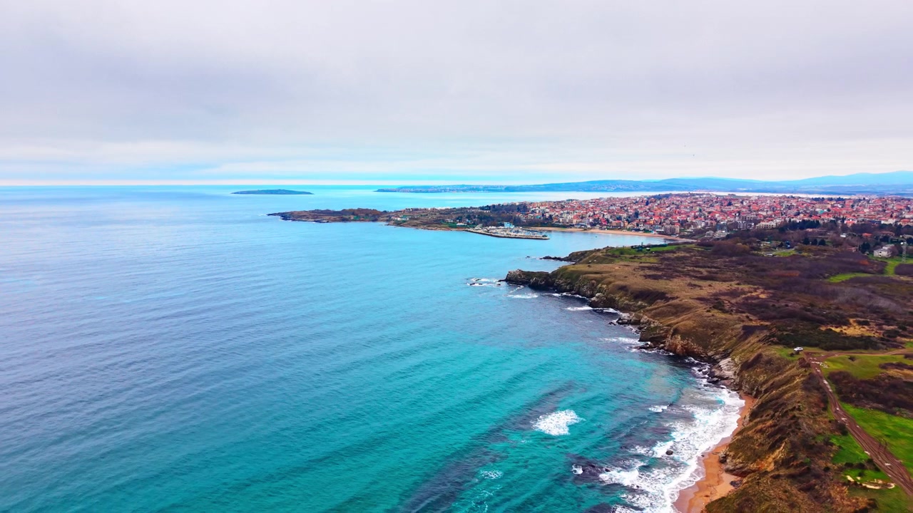 Ripresa panoramica da drone dall'alto di edifici residenziali lungo una baia con mare turchese sotto un cielo nuvoloso. Vista aerea di una città costiera su una penisola, Sozopol, Bulgaria.