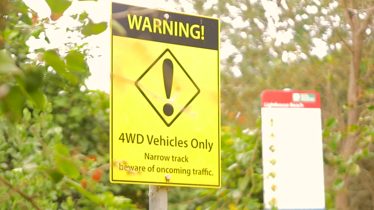 Slow motion close up of warning sign for 4WD driving car vehicles along bushland forest into sandy beach area highlighting risky narrow tracks in Forster Australia rules safety alert and regulations