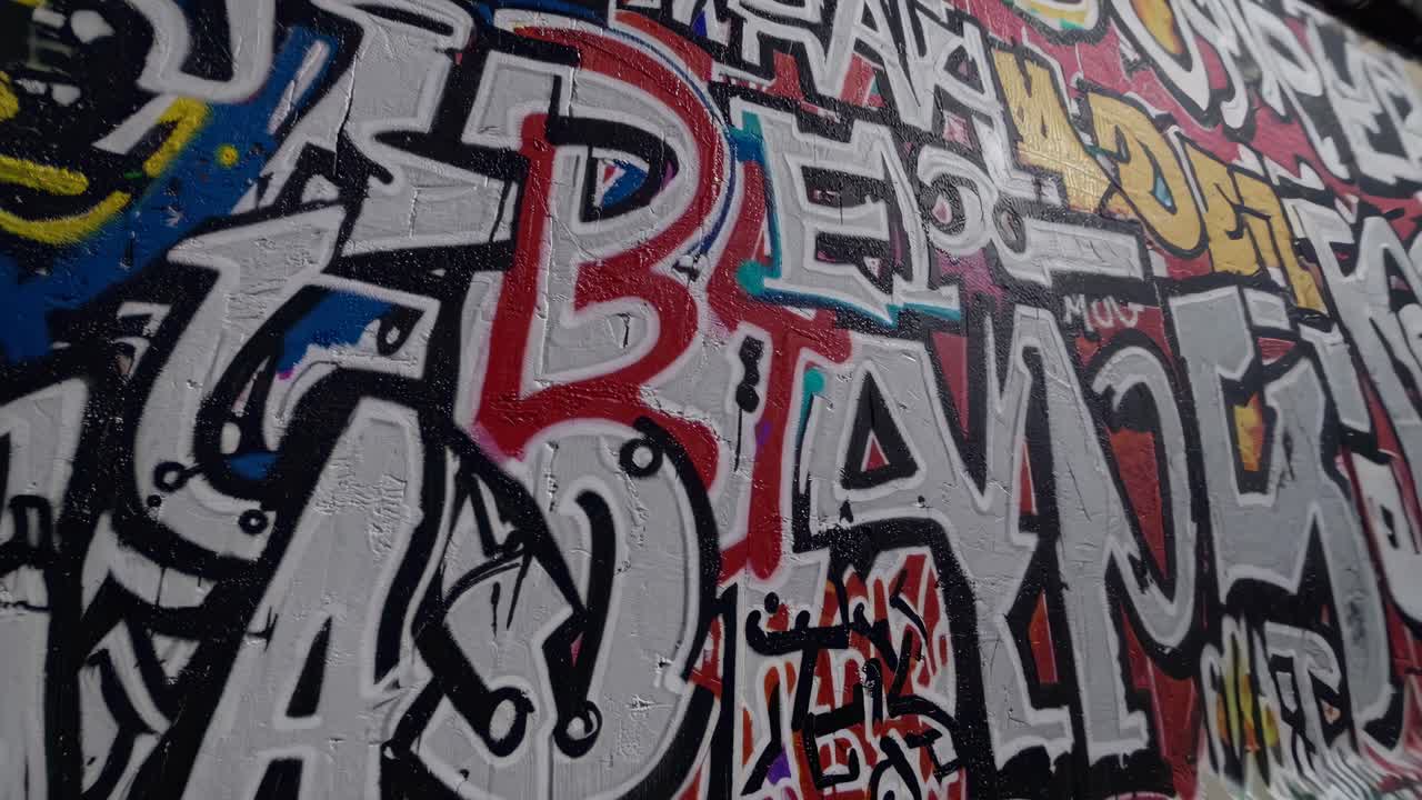 Ripresa video dinamica a livello stradale di un muro ricoperto di graffiti, che cattura l'arte urbana con una prospettiva.