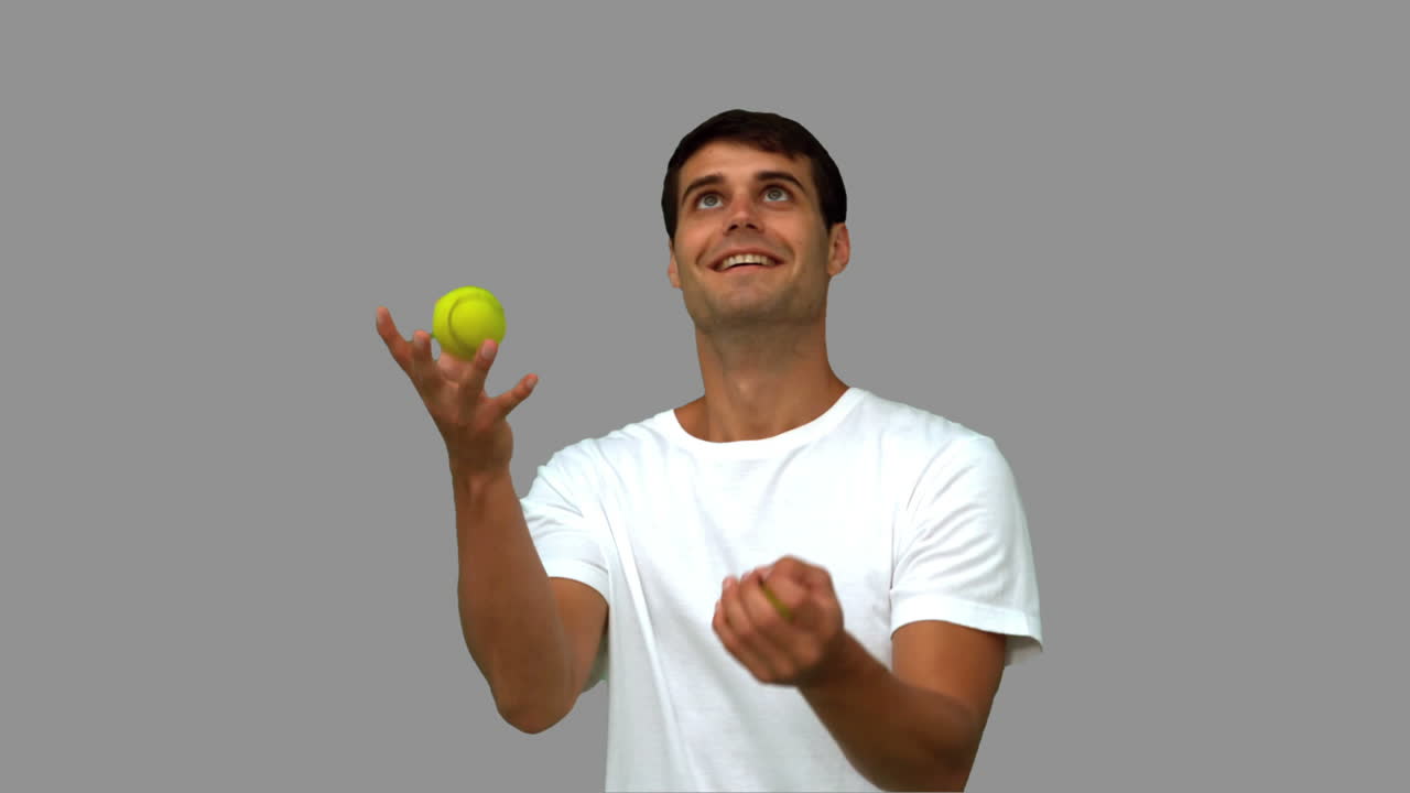Man dribbling with tennis balls on grey screen