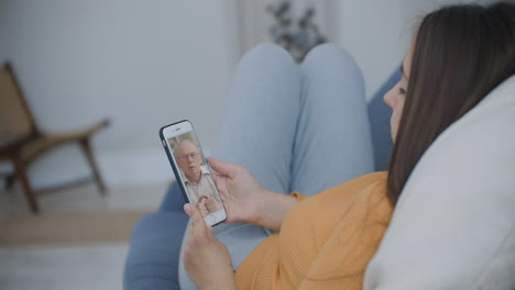 Over-shoulder-view-of-young-woman-daughter-video-calling-old-parent-father-or-mature-friend-using-conference-chat-online-application-on-mobile-phone-screen-at-home-office.-Family-videocall-concept